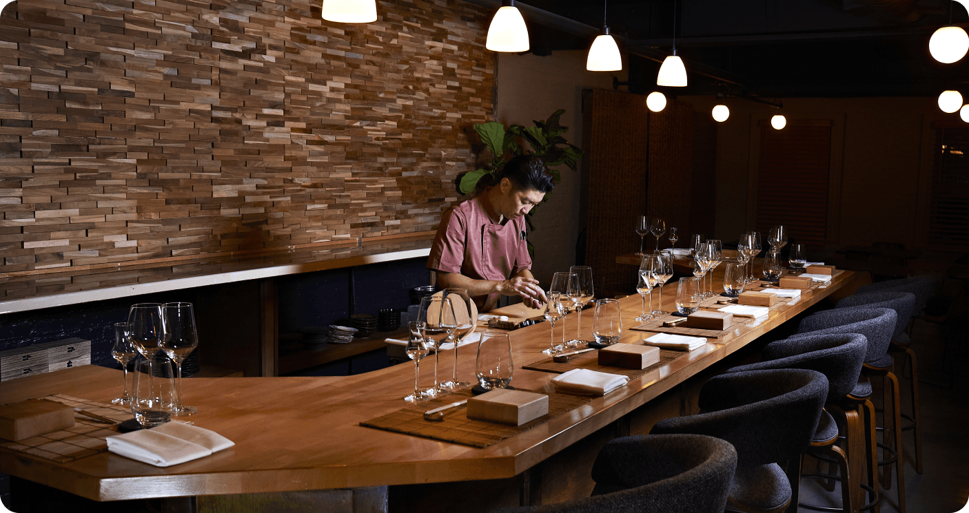 Chef preparing omakase at wooden counter with brick accent wall and pendant lighting