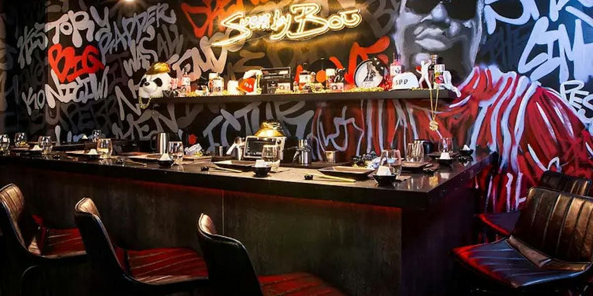 Modern bar with neon signage and graffiti-style wall art, black counter seating