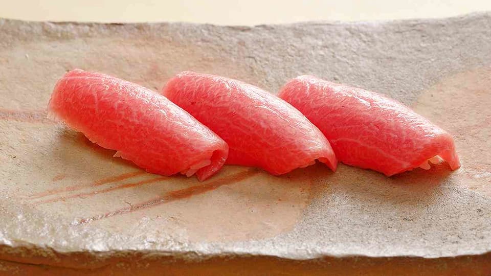 Three pieces of raw tuna nigiri sushi on stone plate