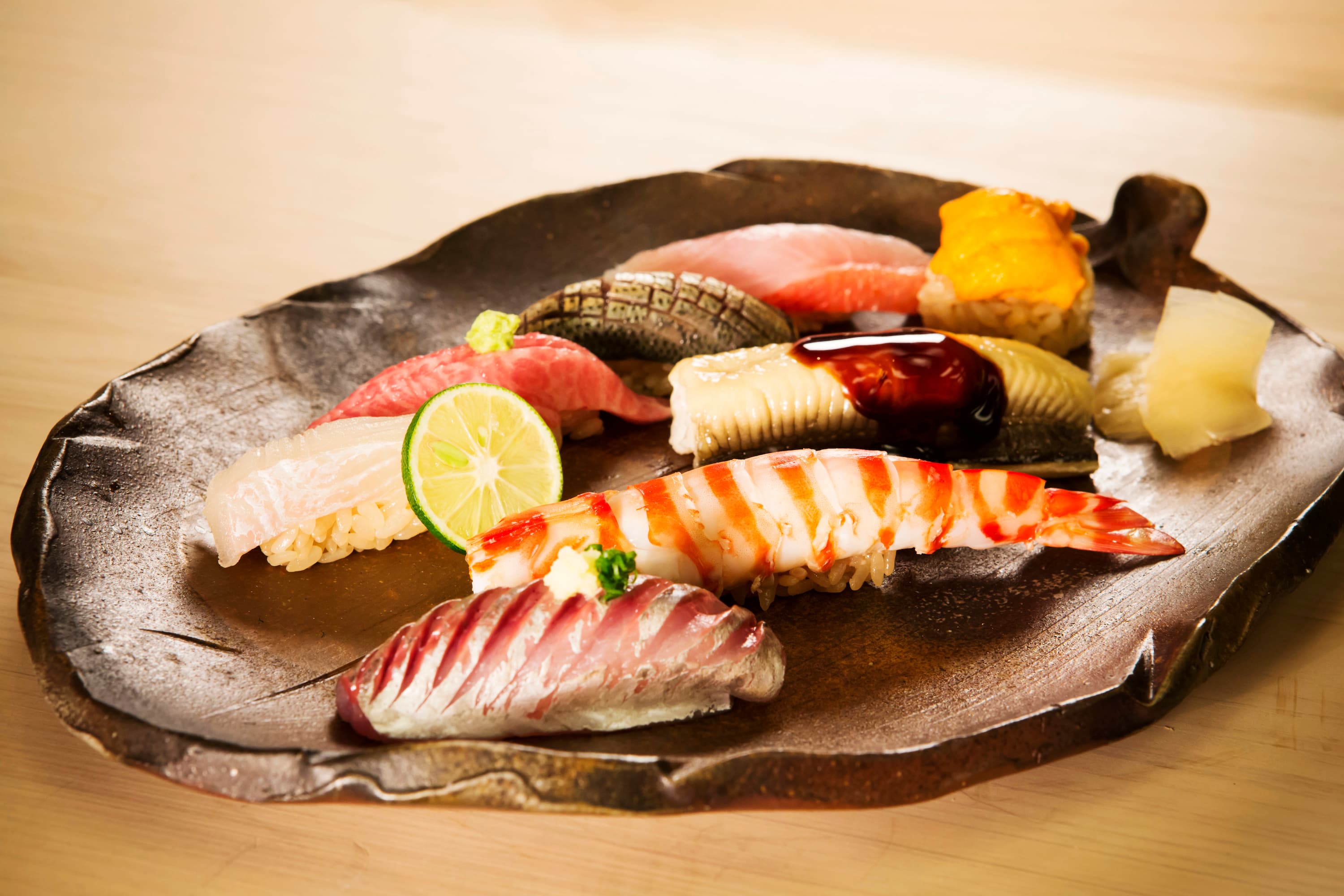 Assorted nigiri sushi on a dark ceramic fish-shaped plate with lime garnish