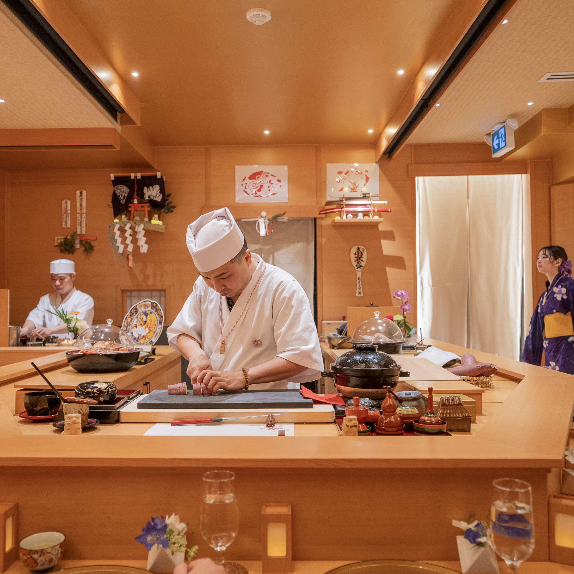 Japanese chef in white uniform and hat preparing food at wooden counter in warm-lit dining room