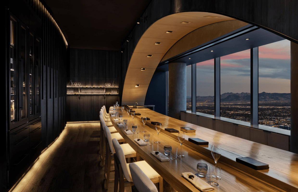 Modern dining room with curved wood ceiling, long table, and panoramic sunset city views