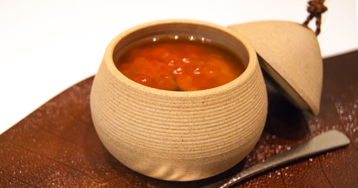 Artfully presented soup in a woven ceramic bowl on brown plate with spoon