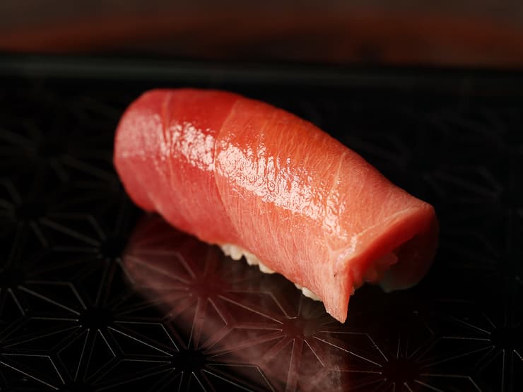 Single piece of raw sushi-grade fish on dark plate
