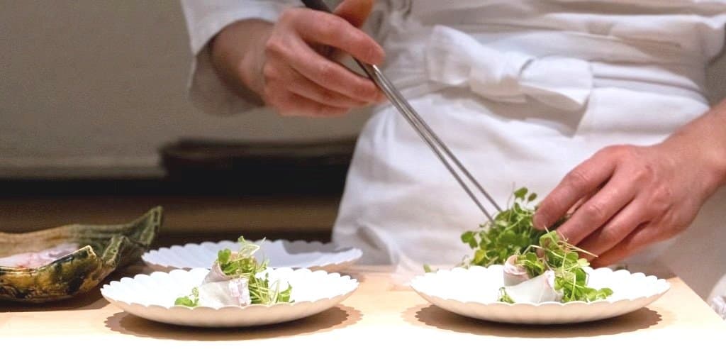 Chef plating delicate dishes with microgreens and garnish