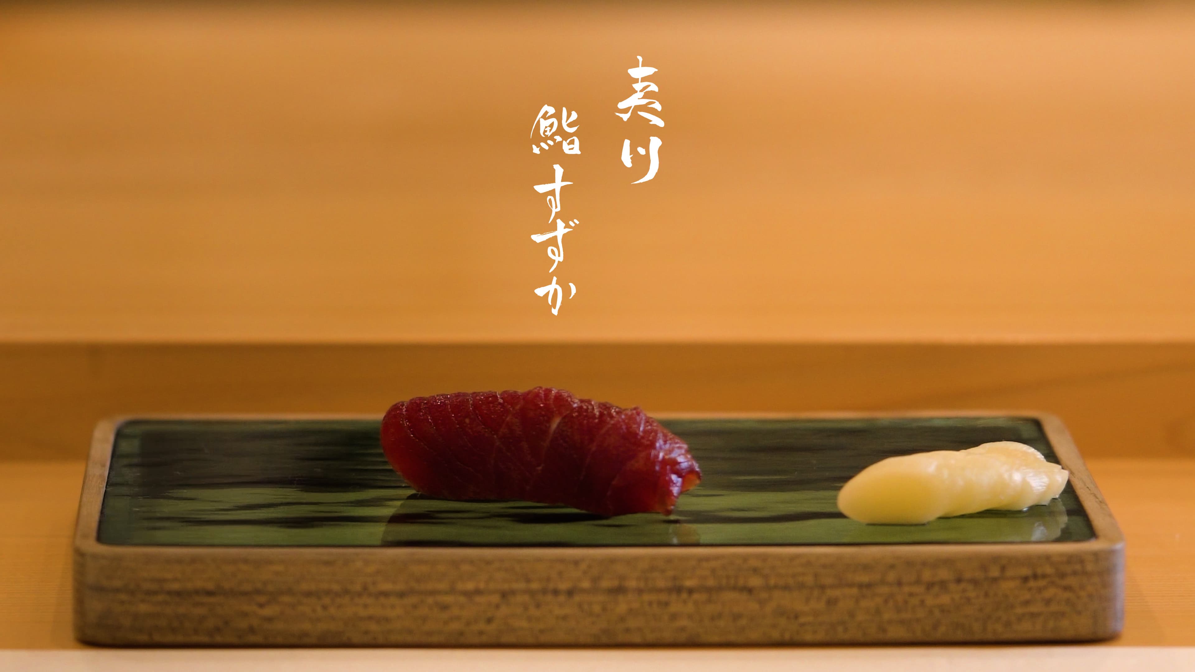 Two pieces of nigiri sushi on a slate plate with Japanese calligraphy banner above