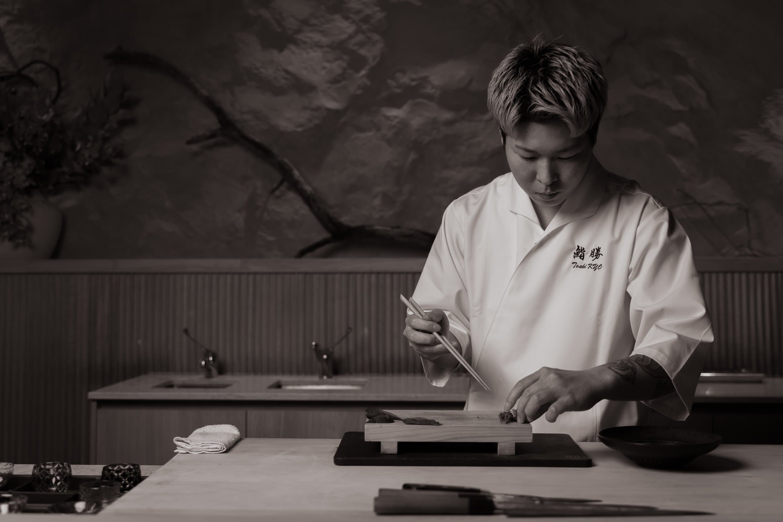 Chef in white chef's coat preparing sushi at wooden counter in minimalist kitchen