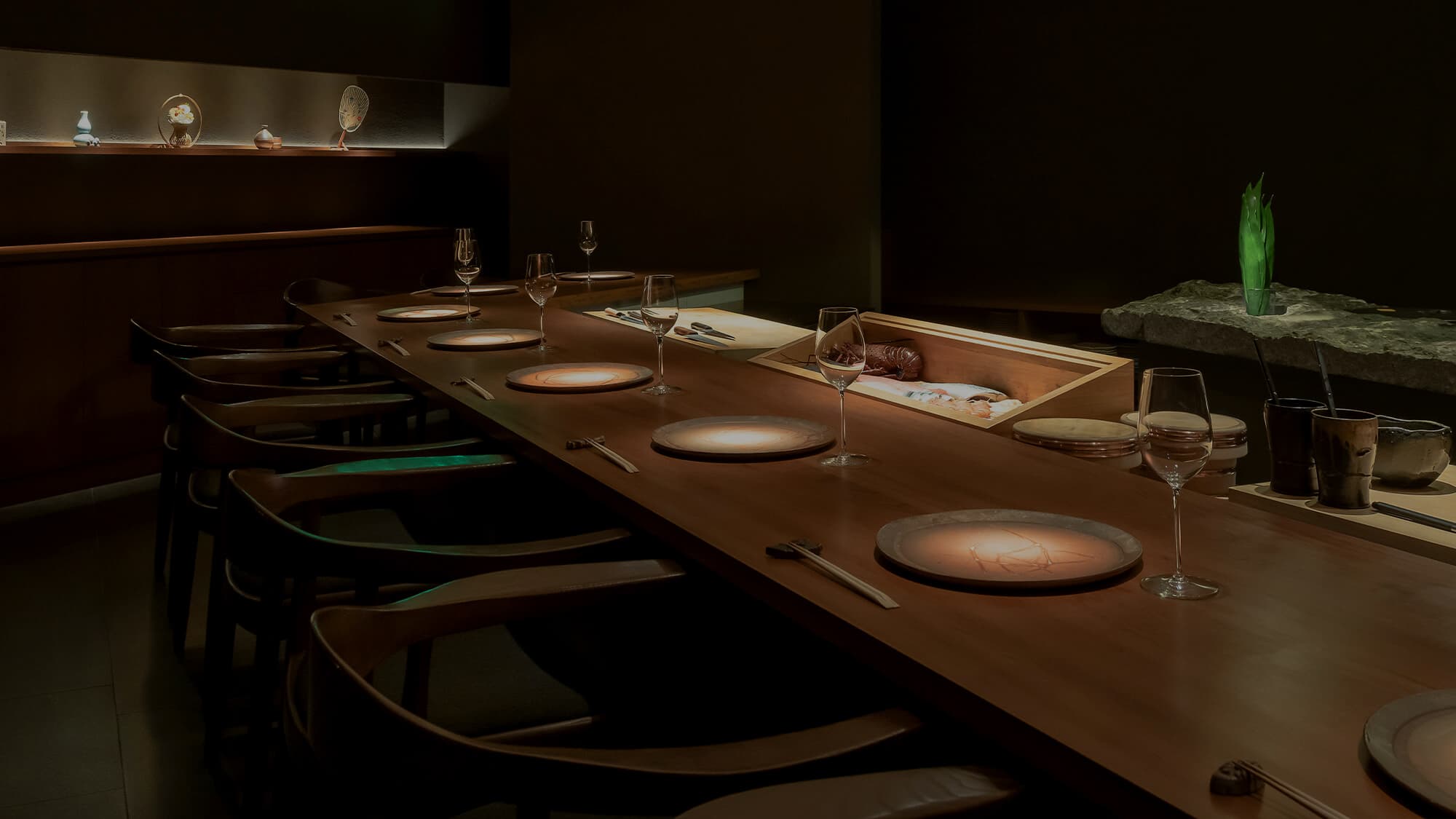 Upscale dining counter set with place settings, wine glasses, and artistic tableware in dim lighting