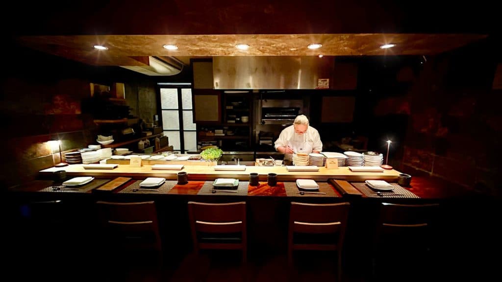Chef at sushi counter with seated diners in intimate restaurant setting