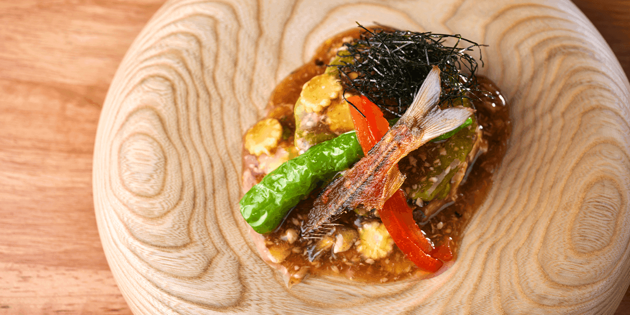 Artfully plated Japanese fish dish with vegetables and seaweed on wooden plate