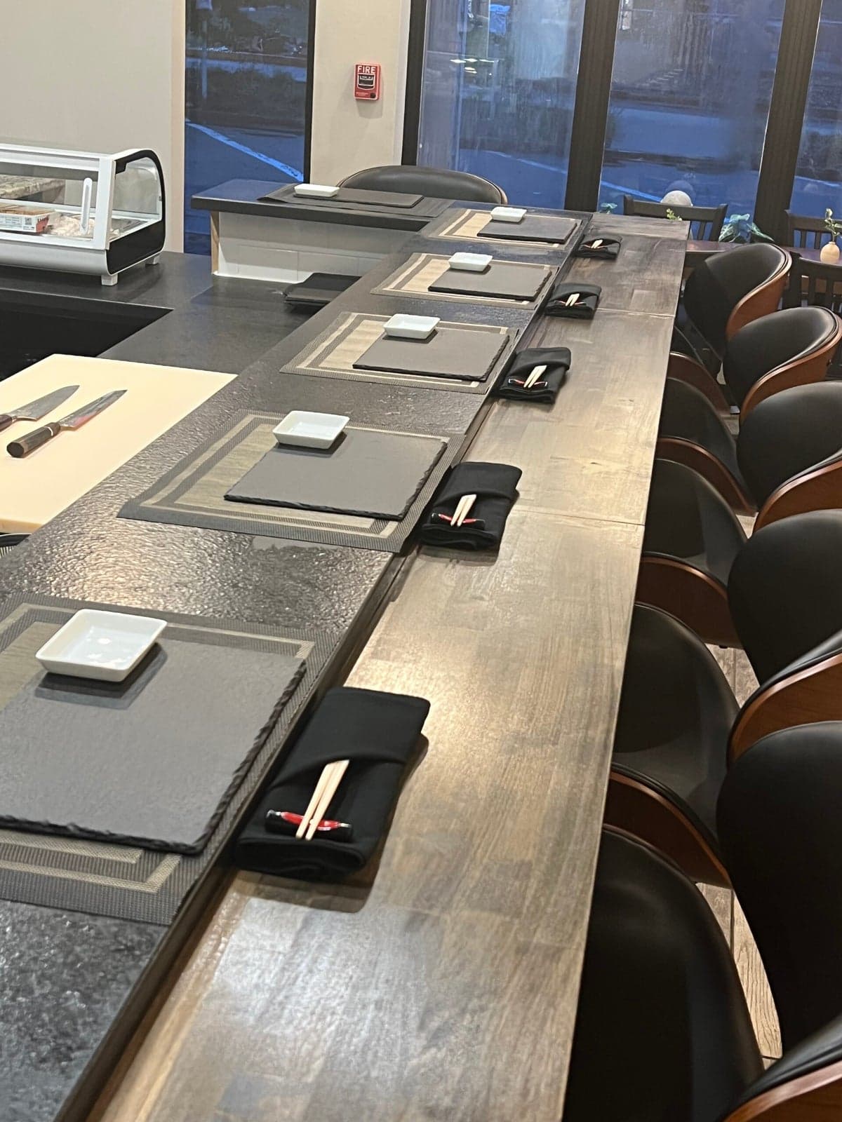 Modern conference room with long wooden table, black chairs, and floor-to-ceiling windows overlooking city lights