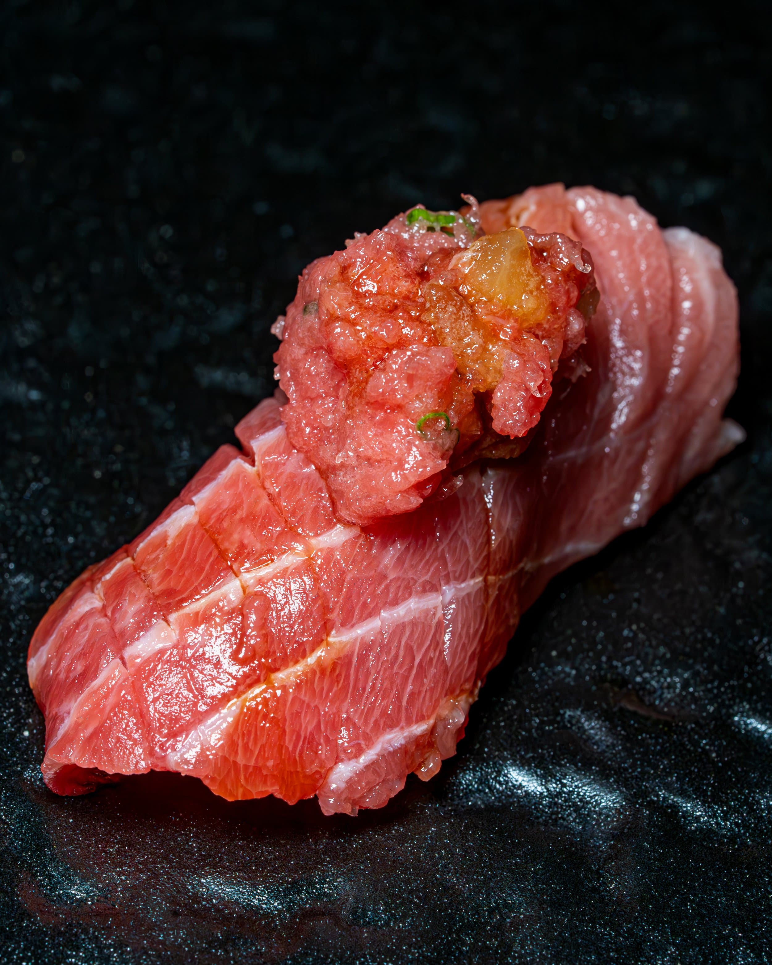 Sushi nigiri with raw fish and garnish on dark surface
