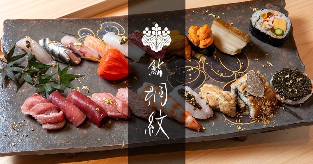 Assorted nigiri sushi and rolls with gold leaf on dark slate platter