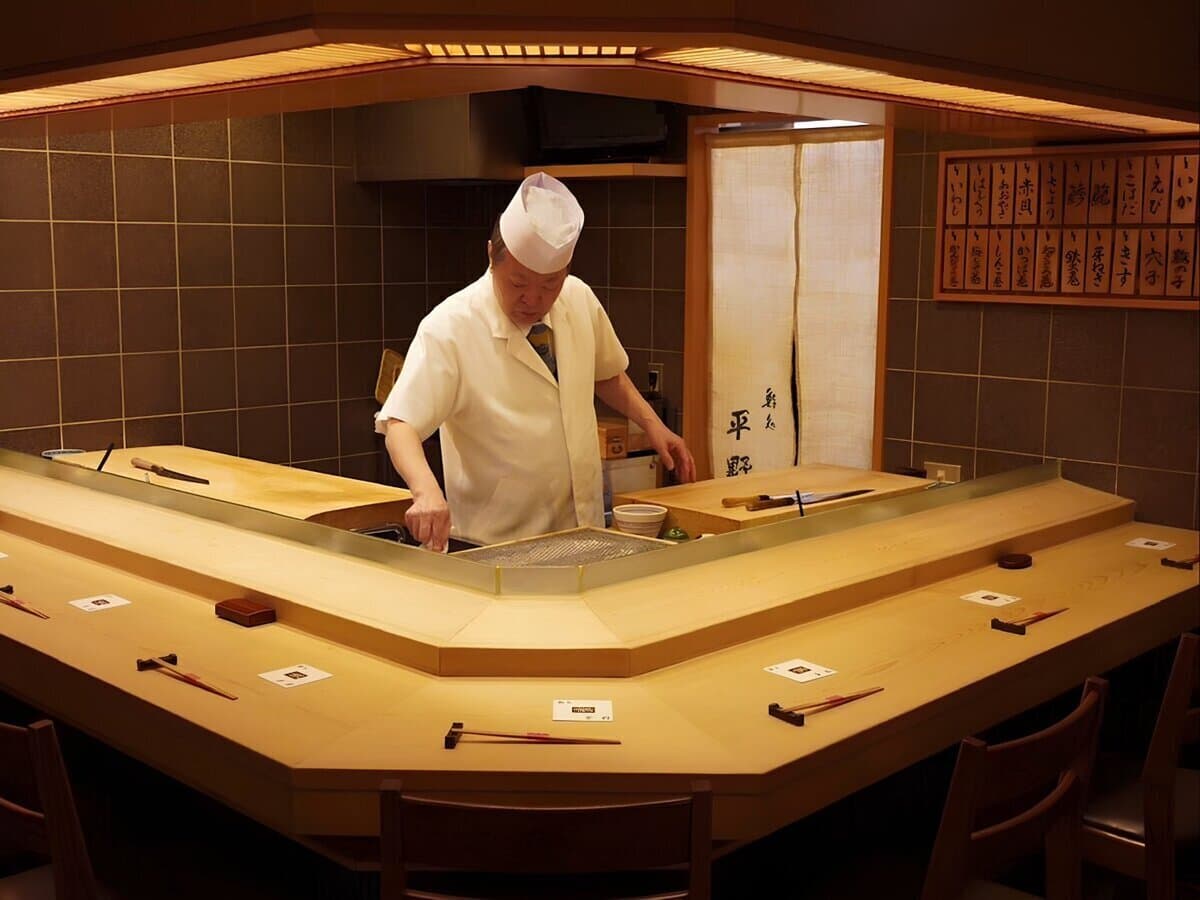 Chef in white uniform and hat preparing food at sushi counter