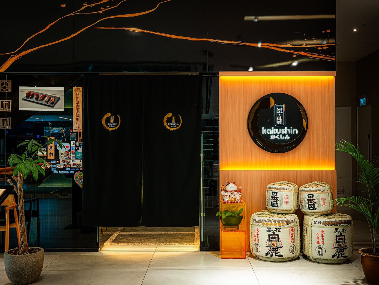 Kakushin restaurant storefront with illuminated orange signage and traditional sake barrels at night