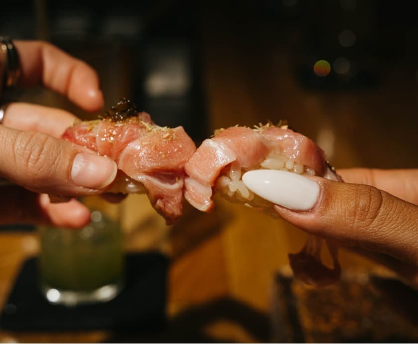 Hands holding sashimi with white sauce and garnish
