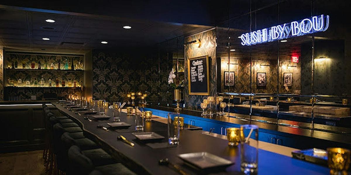 Modern sushi restaurant interior with blue-lit bar, dark damask wallpaper, and neon signage