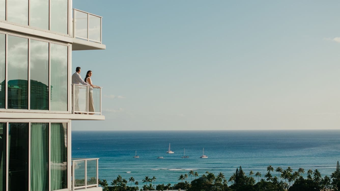 Modern oceanfront building with guests on balcony overlooking sailboats and tropical coast