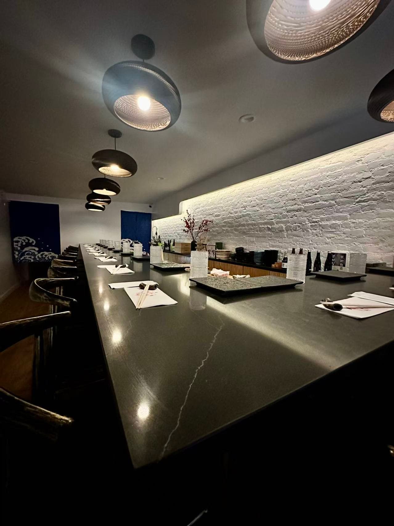 Modern omakase counter with sleek dark marble, pendant lighting, and white brick accent wall