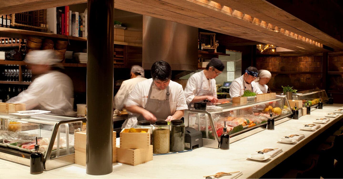 Open kitchen with chefs preparing food at counter with fresh ingredients and ingredients displayed