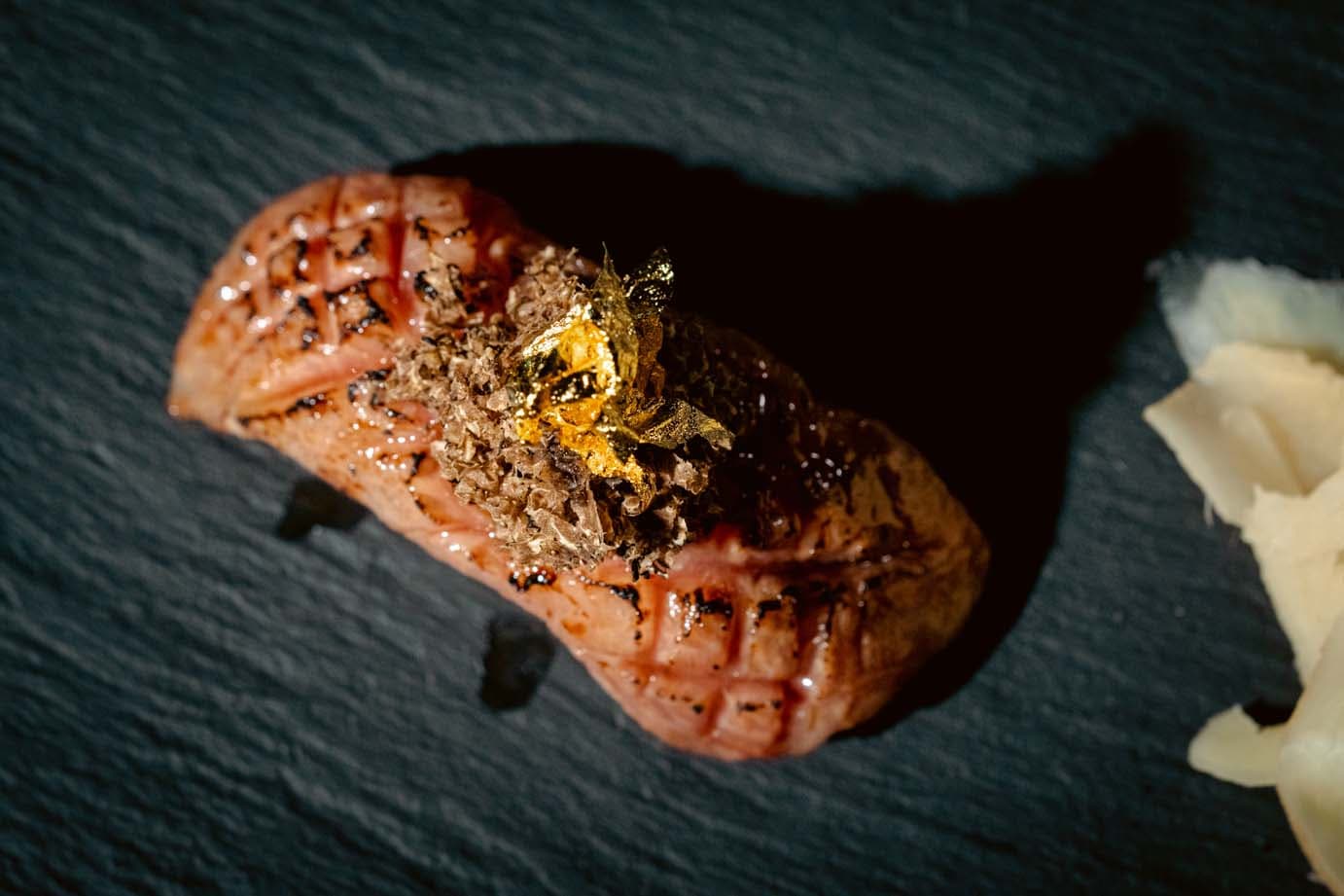 Elegantly plated meat dish with gold leaf and sauce on dark slate