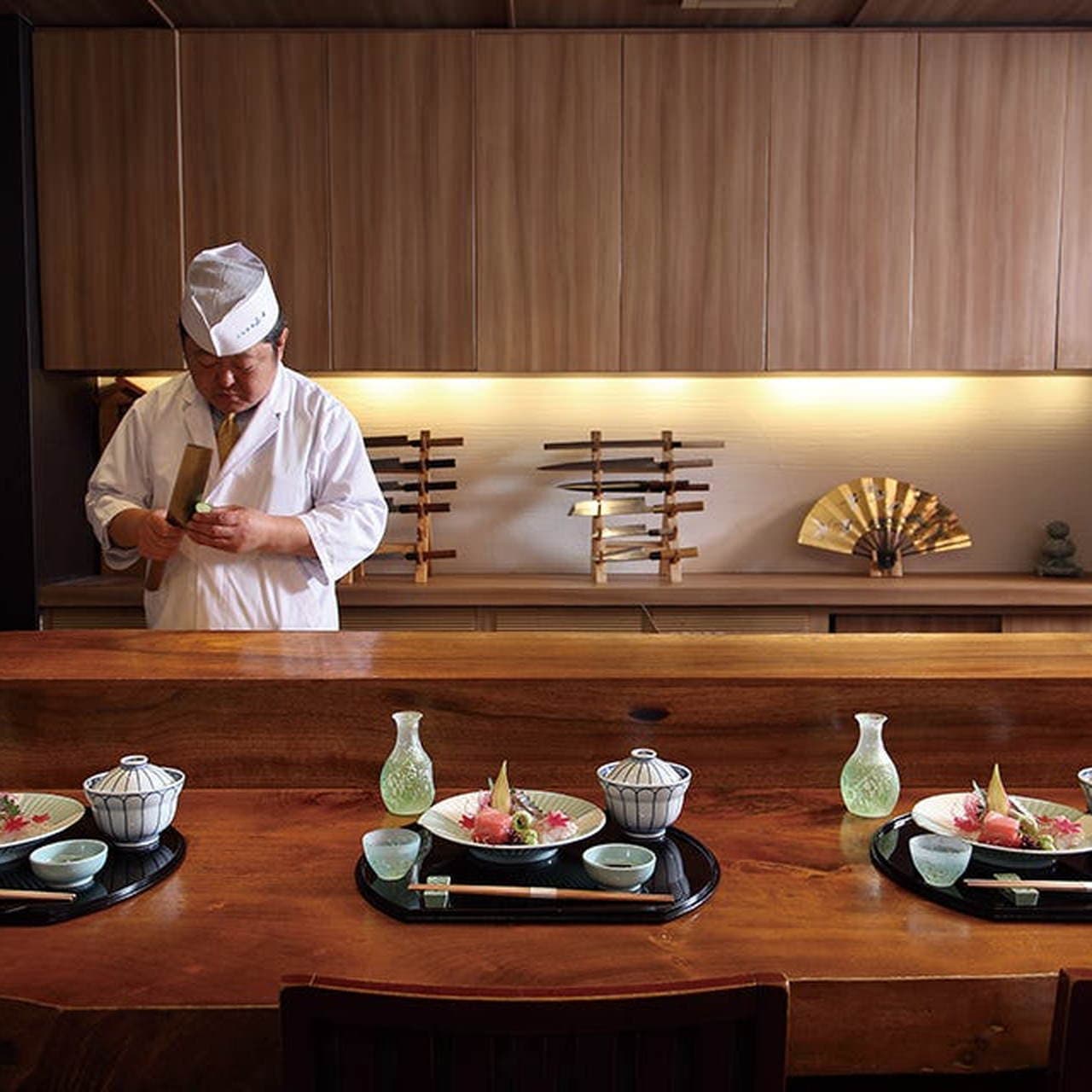 Chef in traditional white garb preparing kaiseki cuisine at wooden counter with plated dishes