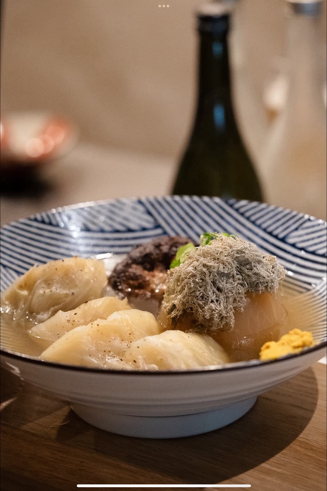 Artfully plated seafood and meat dish with garnish and wine bottle in background