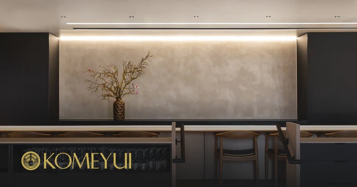 Modern restaurant interior with KOMEYUI logo, minimalist black and beige design, and decorative branch arrangement
