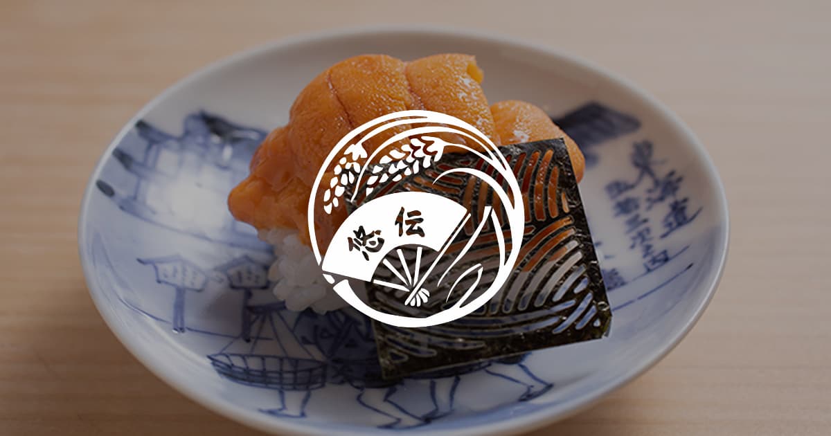 Plated sushi with fried items on decorative blue and white ceramic plate with logo overlay