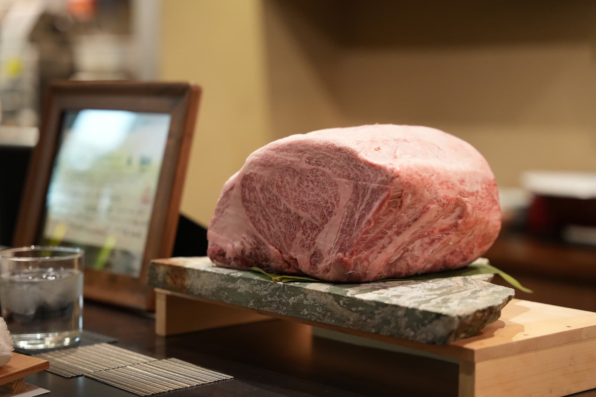 Raw beef cut displayed on slate with garnish and glass of water on wooden table