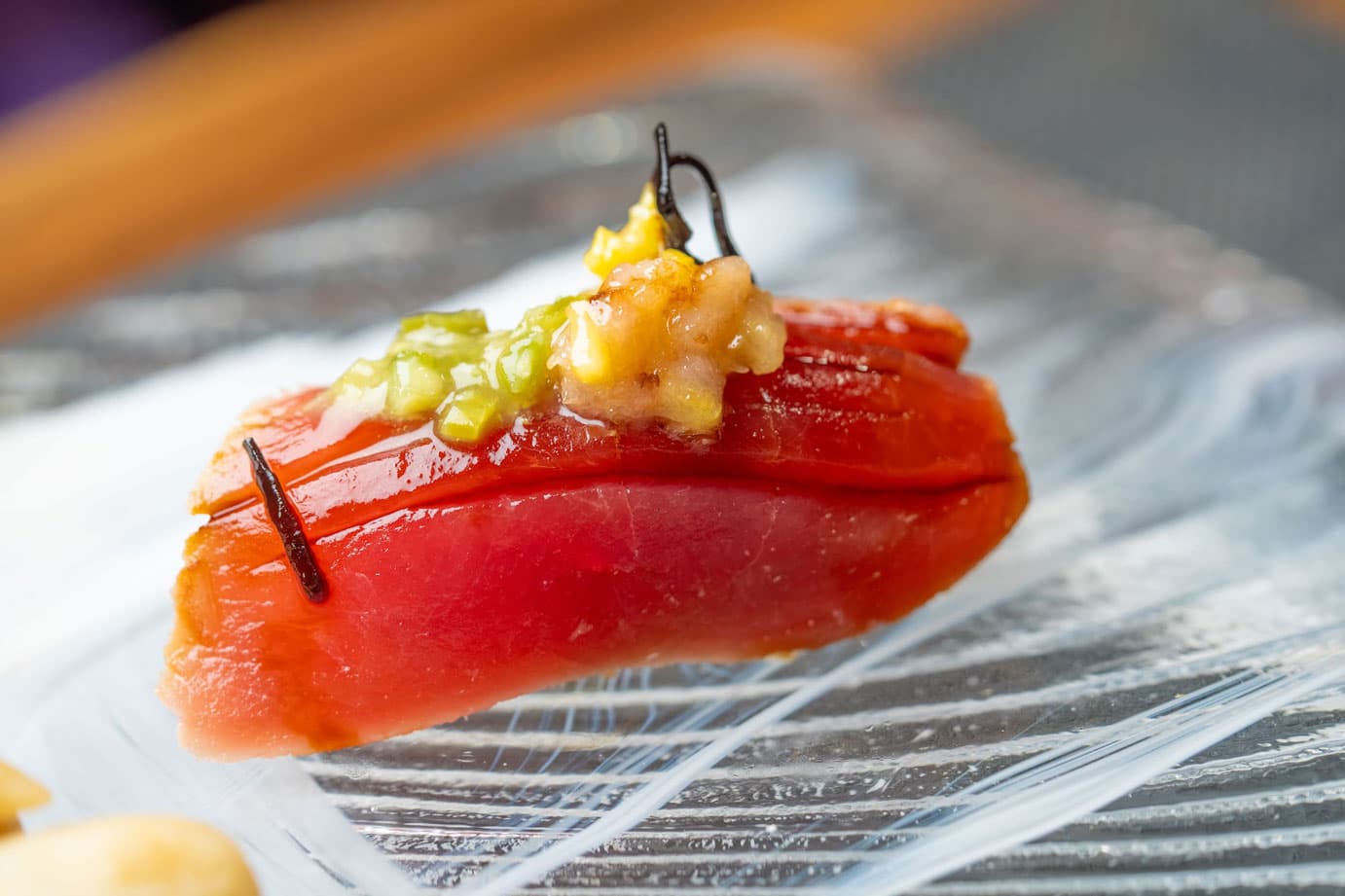 Sashimi slice with yellow garnish and dark skewer on decorative plate