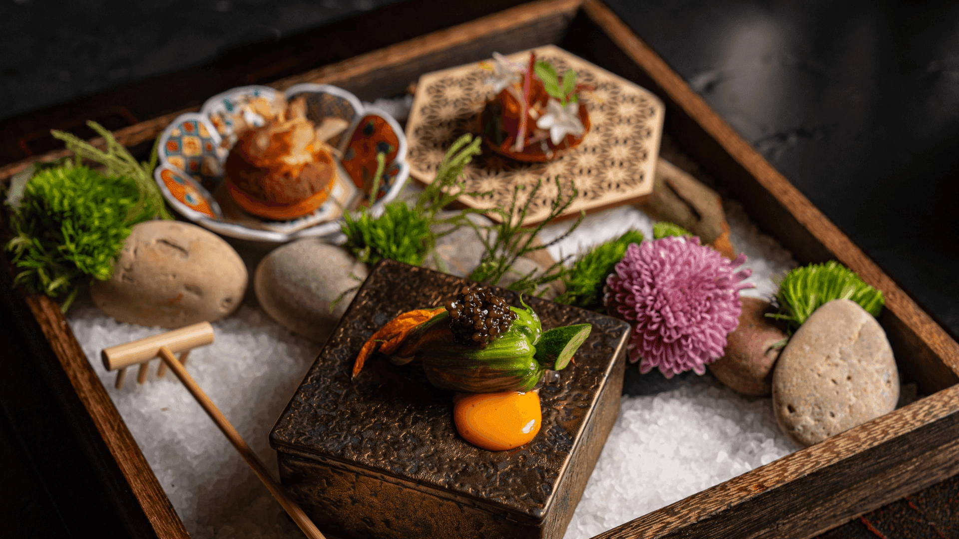 Artfully plated Japanese dishes on wooden tray with flowers and decorative elements