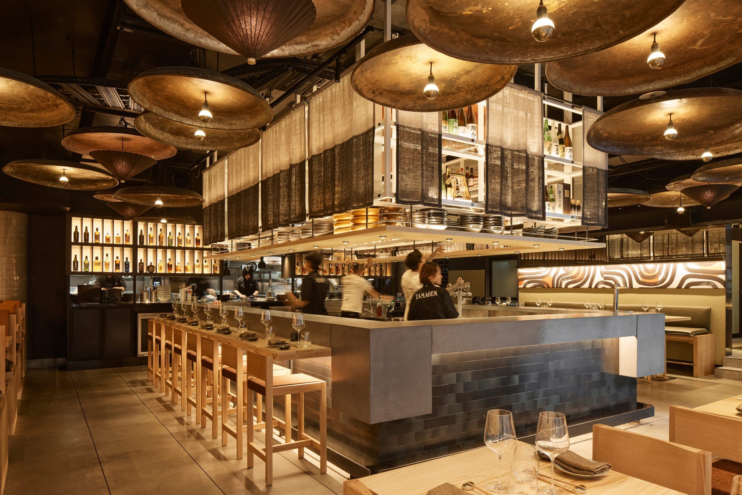 Modern restaurant interior with brass disc ceiling lights, bar seating, and open kitchen concept