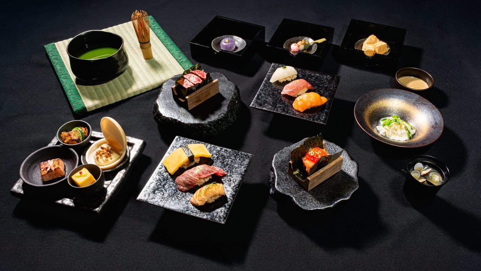 Elegant omakase spread with sushi, sashimi, matcha tea, and sauces on dark surface
