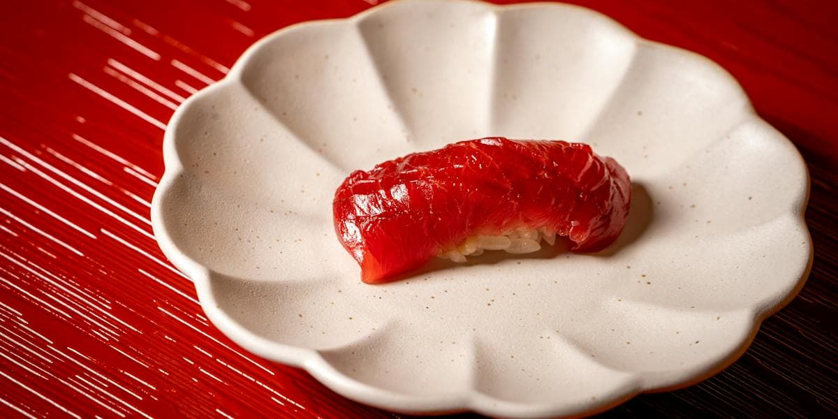 Single piece of nigiri sushi with red fish on decorative white plate