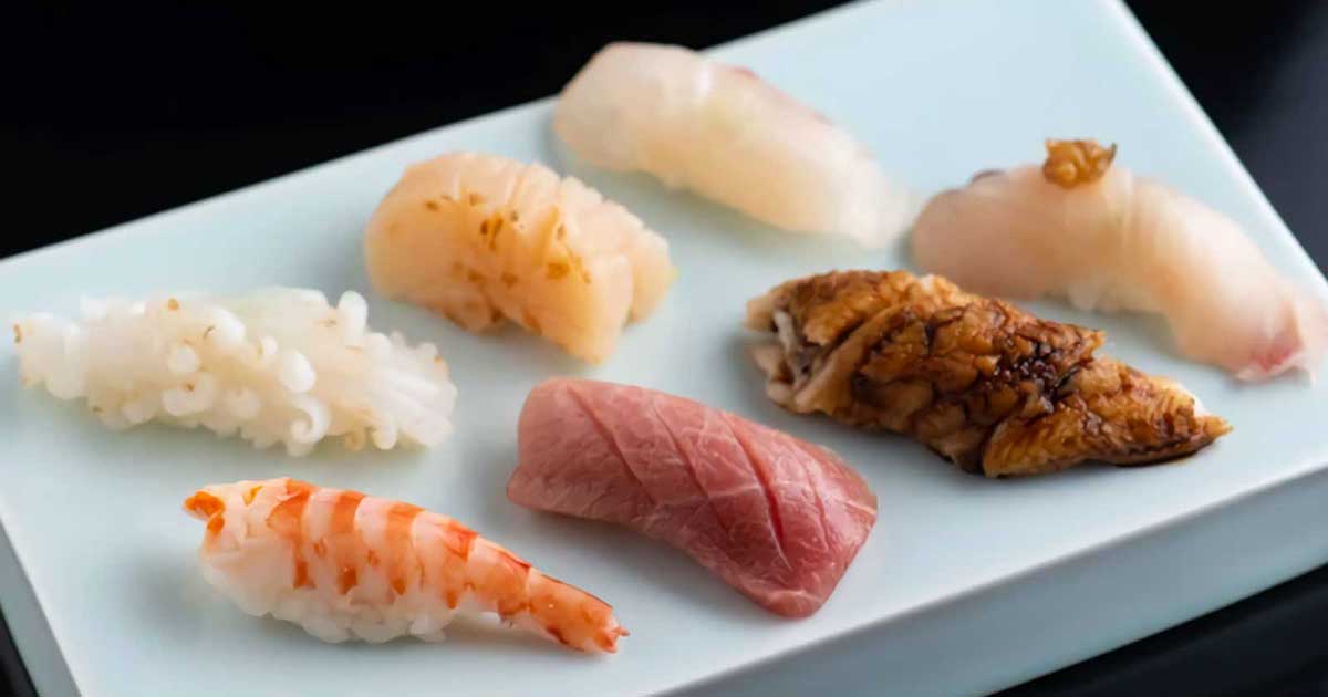 Assorted sushi and nigiri on a white plate including shrimp, scallop, and red fish