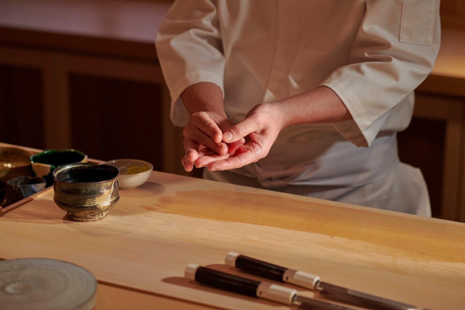 Chef's hands preparing sushi over wooden counter with traditional tea bowls