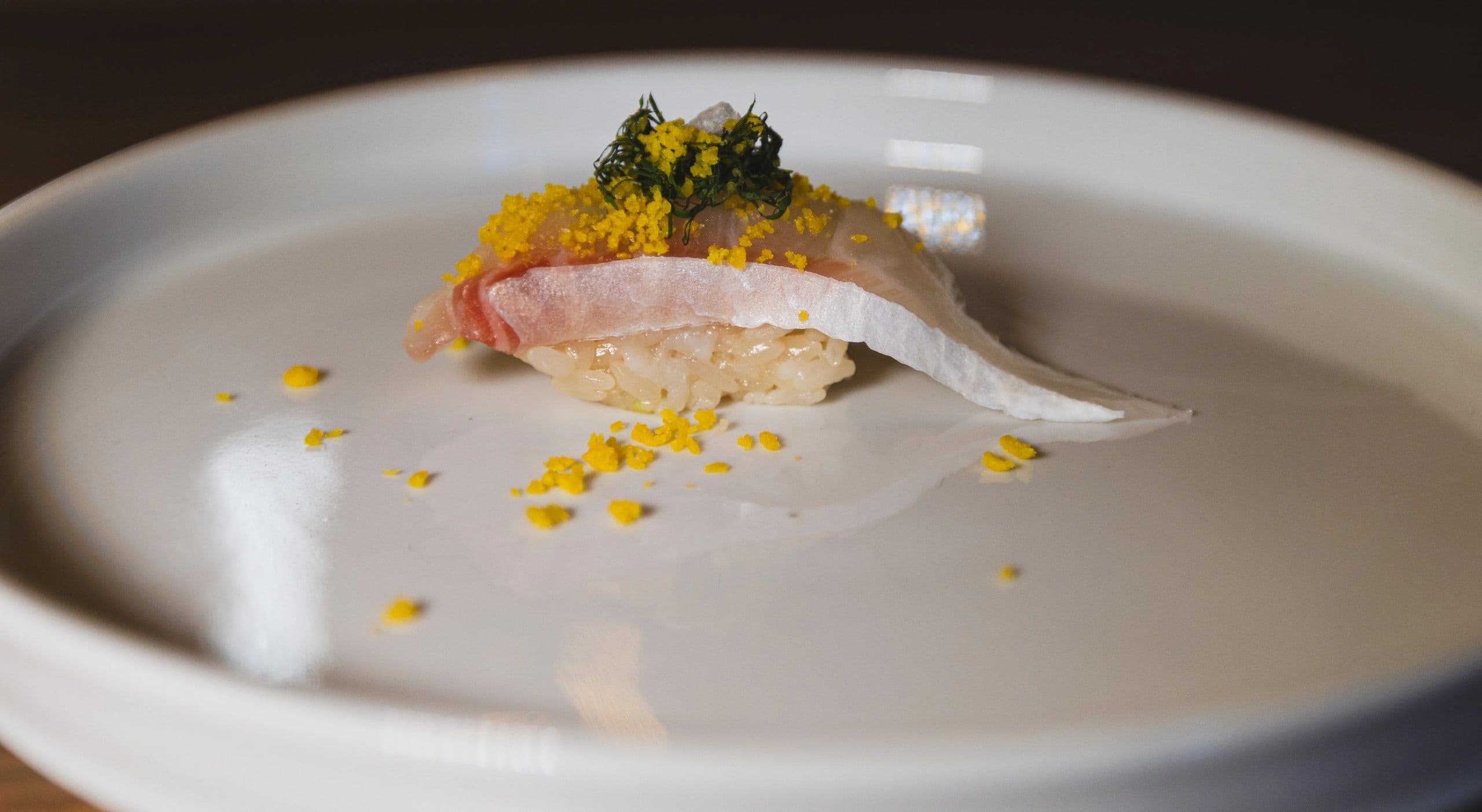 Elegantly plated nigiri sushi with uni, topped with yellow roe and garnish on white plate