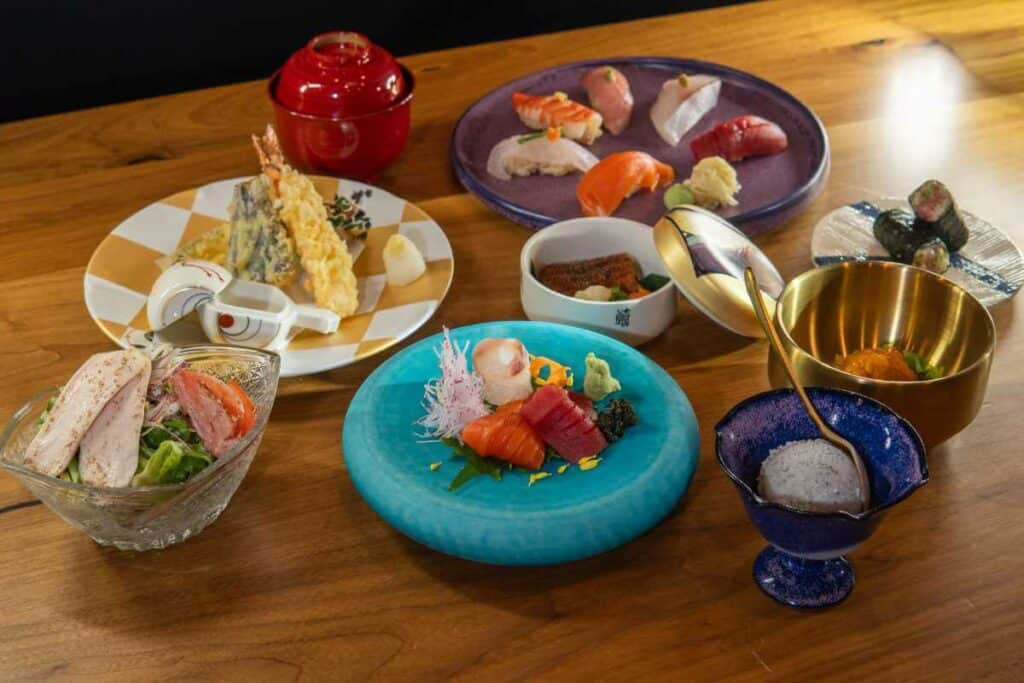 Japanese omakase spread with sashimi, nigiri sushi, tempura, and garnishes on wooden counter