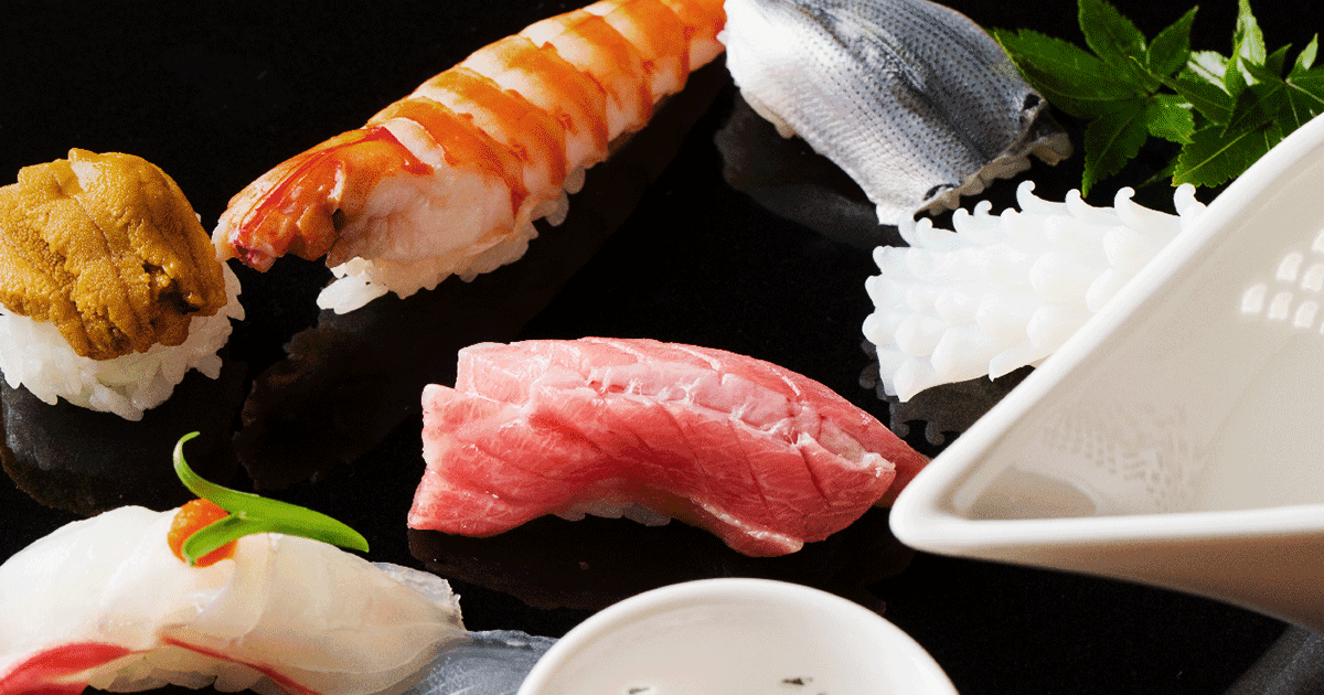 Assorted nigiri sushi including lobster, tuna, and sea urchin on black surface