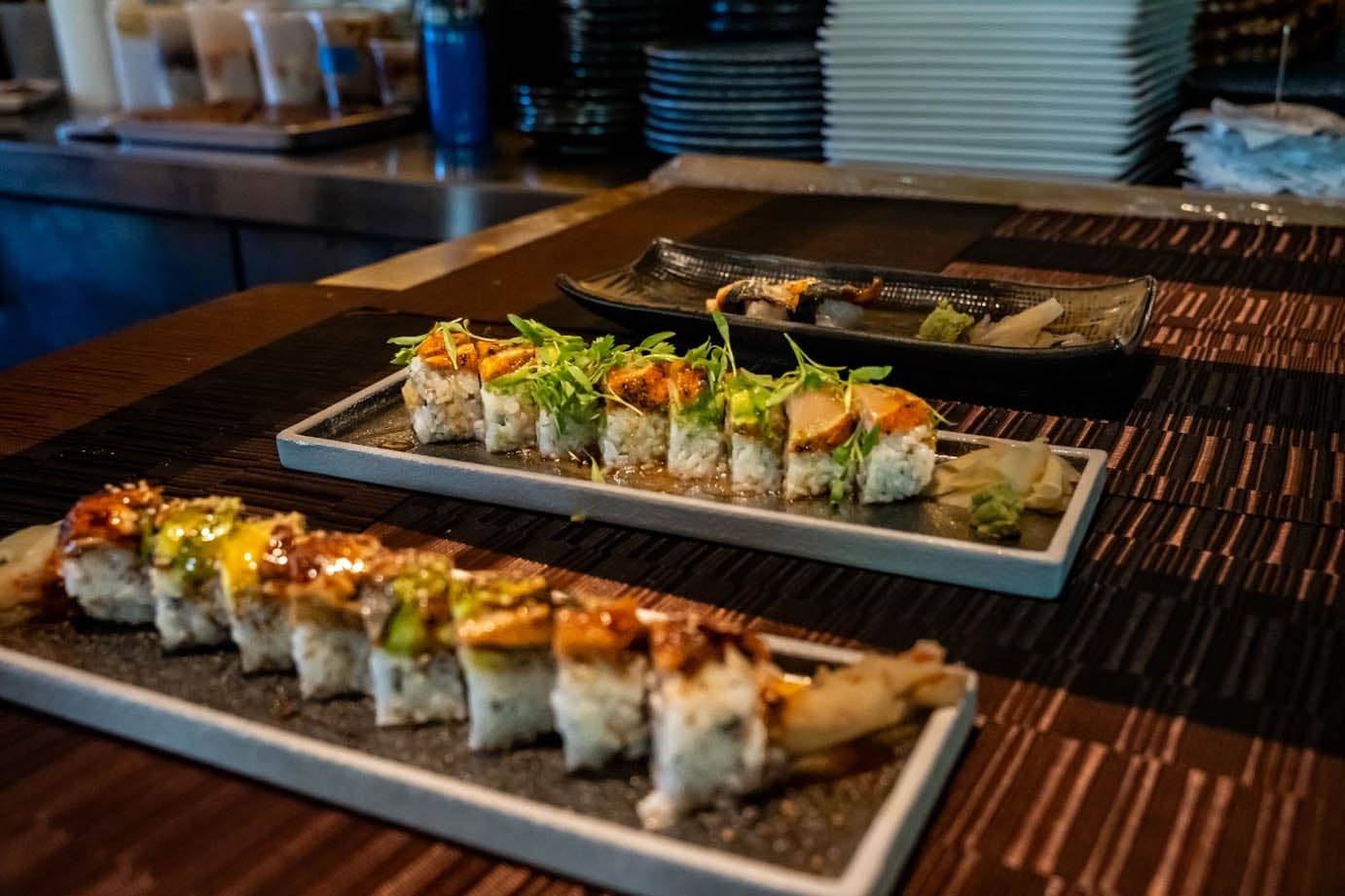 Plated sushi rolls with orange and yellow toppings arranged on white rectangular dishes