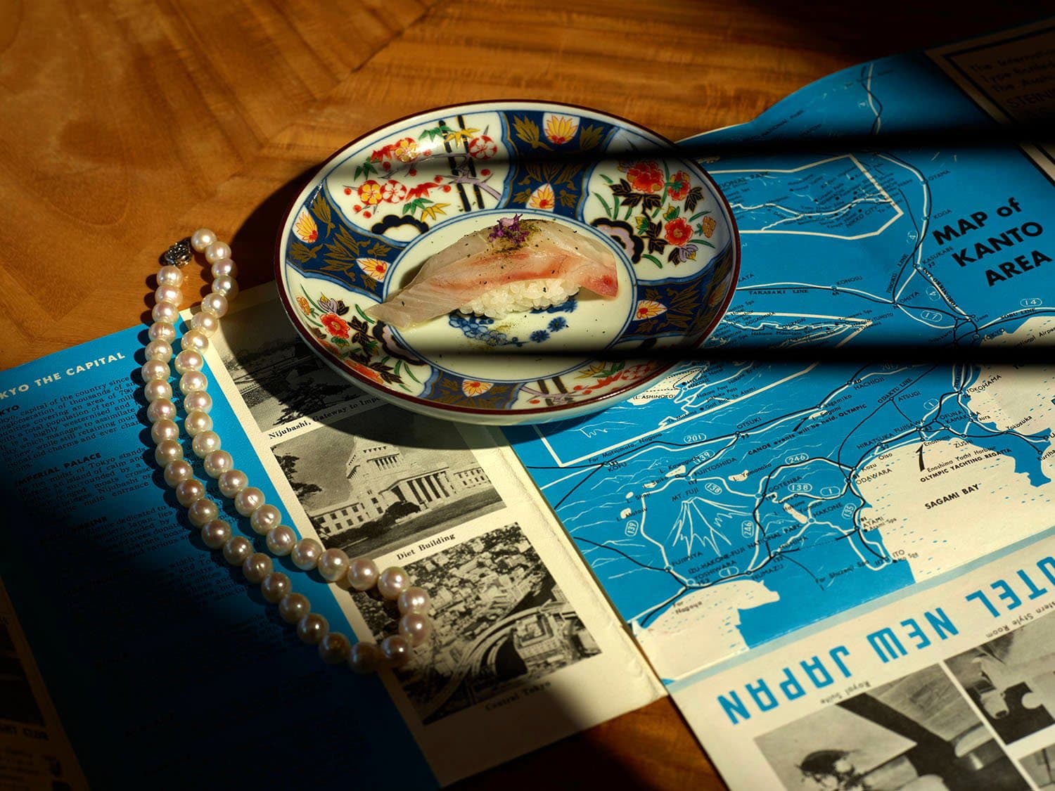 Sushi on decorative porcelain plate with map and pearls on wooden surface