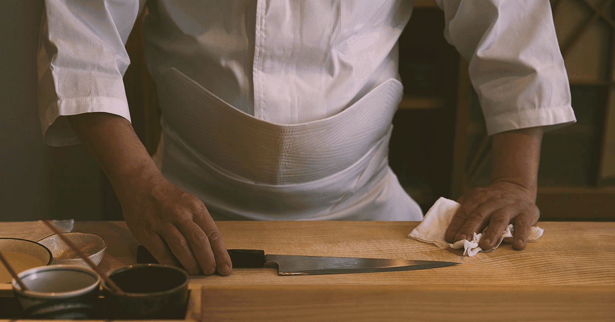 Chef's hands preparing food at wooden counter with knife and ingredients