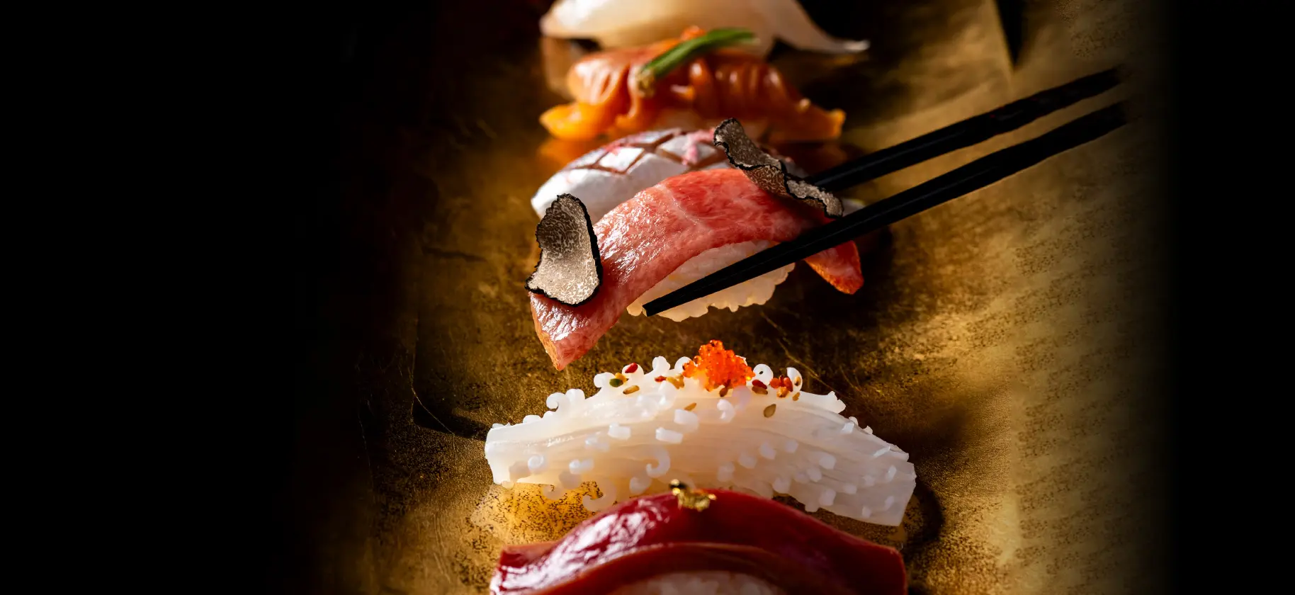 Sushi chef using chopsticks to place truffle on nigiri with raw fish and rice
