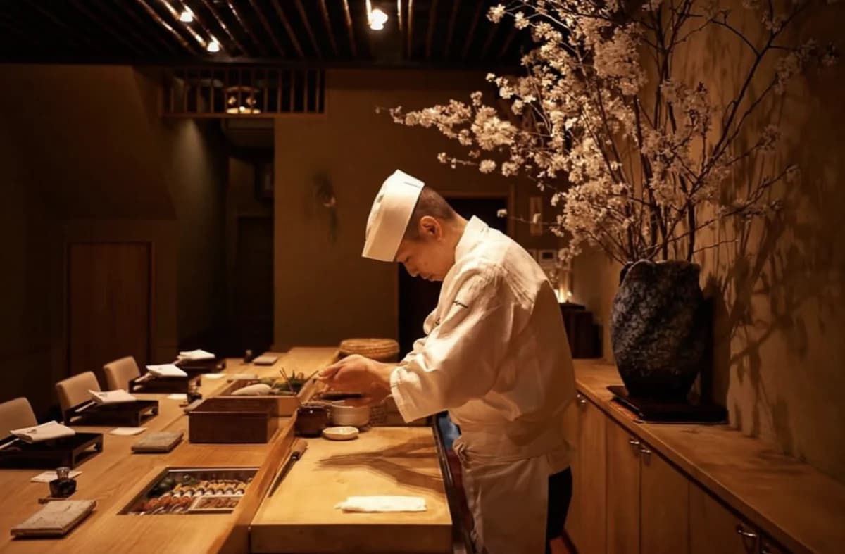 Chef in white uniform and headband preparing food at wooden counter with dried flowers